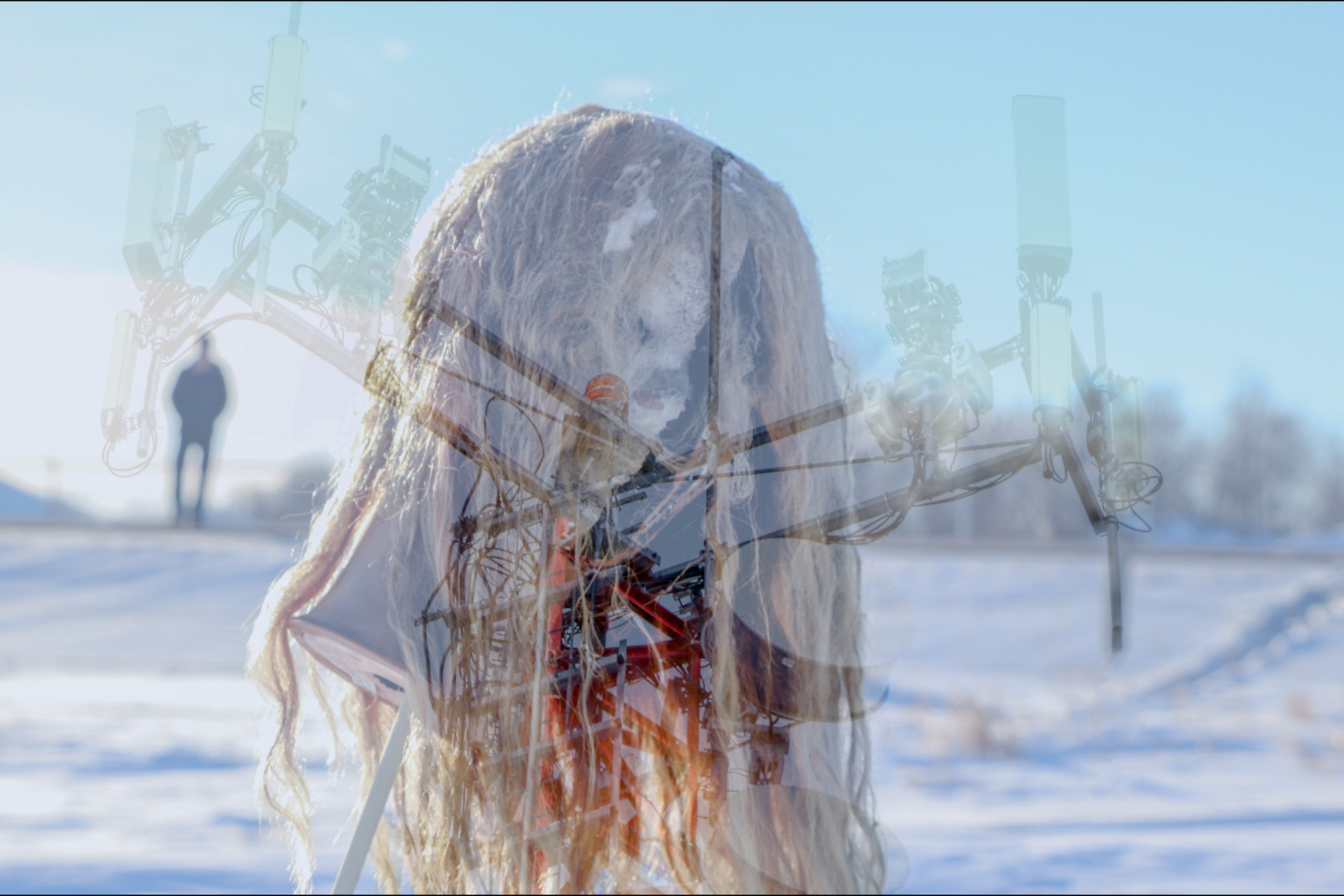 The background of this image is cold and white, like a snowscape.  Front and centre is a disturbing figure: a matted, stringy blonde head of long hair gives the suggestion of a human upper body.  Superimposed is a translucent cell tower structure, its technical, sharp angles creating a harsh juxtaposition to the organic form of the figure.    Unsettlingly, the dim silhouette of a second figure stands motionless and unfocussed on the horizon to the left.