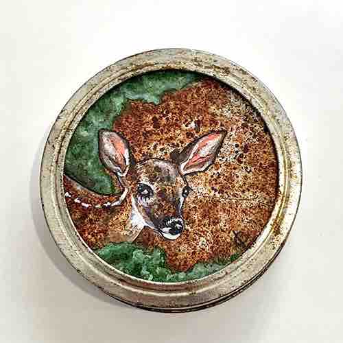 Painted on a rusted canning ring top, a fawn’s head and shoulders emerge into view from green foliage. The mottled brown of the deer’s coat is echoed in the mottled brown of the rusted metal backdrop.