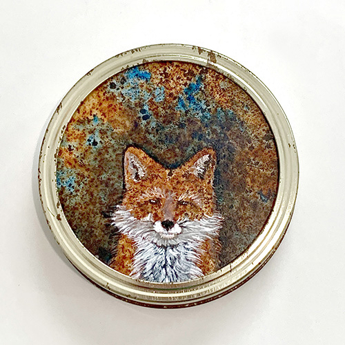This canning lid is rusty brown and turquoise. From the foreground, a red fox with a white breast and whiskers stares directly at us.