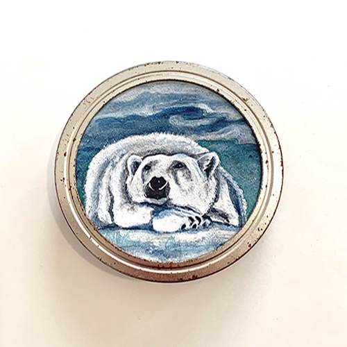 This is a painting of a polar bear relaxing on a bed of snow/ice. Its head is resting on its front paws and its eyes, beady and black, look up and to the side, providing a wistful expression. The tones of the painting are cool, blue and white. The artist paints on the rusted tops of discarded canning rings.