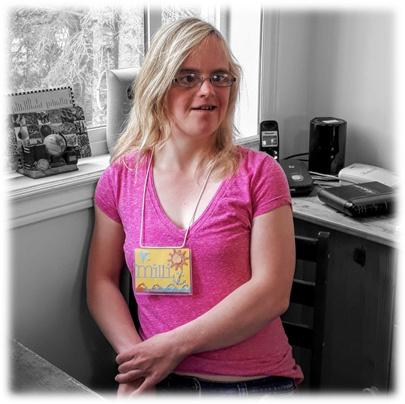 This is a photo of Milli. Millie is a young white woman with blonde hair. She is smiling slightly and looking off in the distance. She is wearing glasses, a bright pink t-shirt and a name tag with her name against a bright yellow background.
