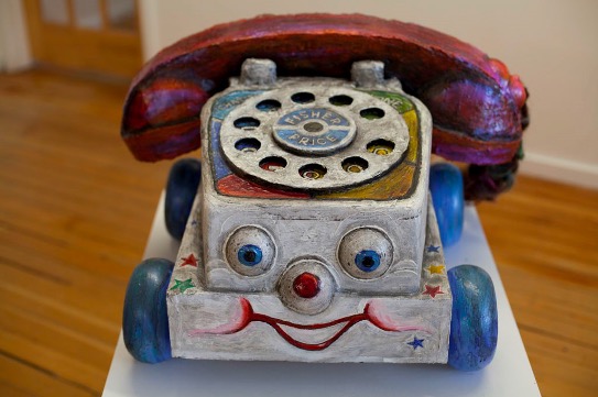 This is a large-scale model of a children’s you phone. The phone is white, blue and red with more colours where you select the numbers. The phone has a smiling face.