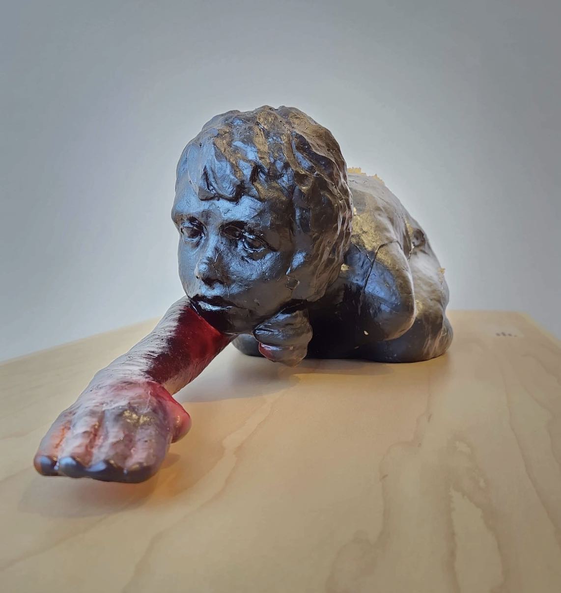 This is a cast glass sculpture. The figure is a young girl, crouched tightly on the ground, knees tucked up under her chest.  One arm is extended forward, delicately exploring the feel of the ground in front of her.  Her other hand supports her chin; on her face is a quizzical, slightly concerned expression of intense concentration.  The figure is 27” from fingertip to toes, and cast in a dark amber-coloured glass.