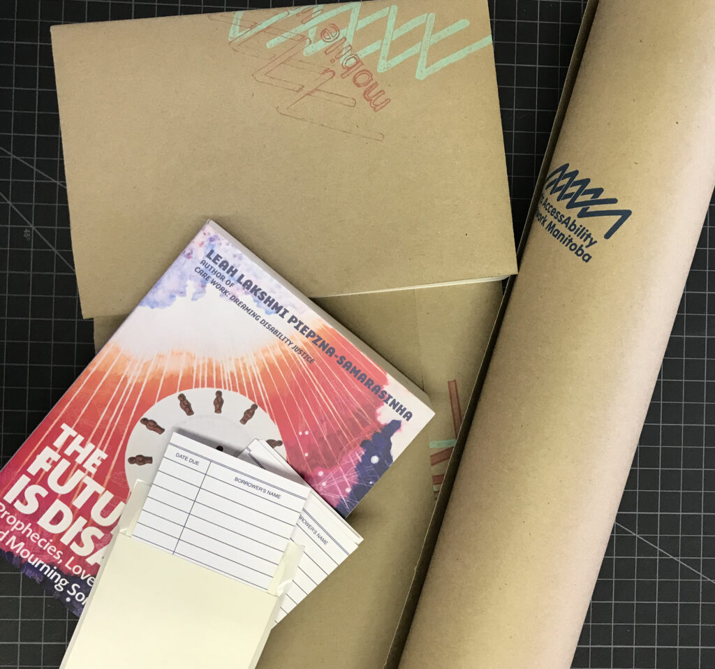 This is a photo of. the packing materials for the mobile lending library. There is a roll of brown paper with AANM's logo on the right, a book wrapped in brown paper in the upper left corner, book with the title "the future is disabled" in the middle of the image with a stack of library cards over.