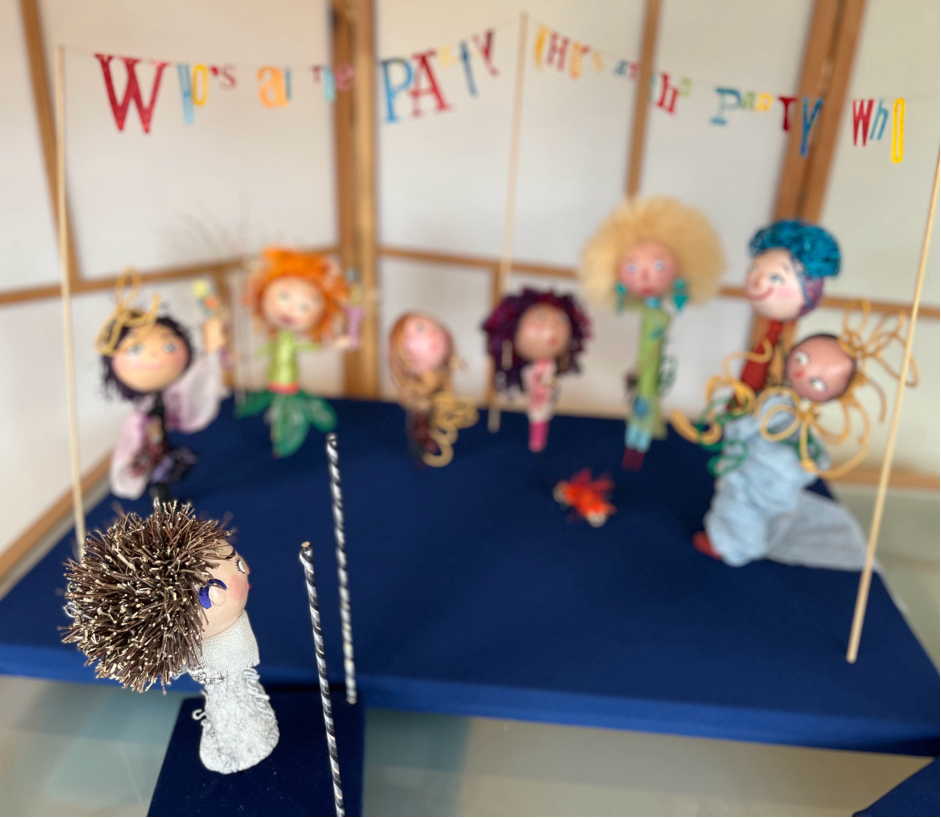 The seven party figures, orange caterpillar and the sign above with colourful letters reading “Who’s At The Party” are very blurred. Alice is in sharp focus. 