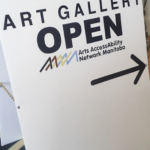 photo of AANM Gallery sign, sporting the AANM logo, the word OPEN, and an arrow pointing to the gallery entrance.